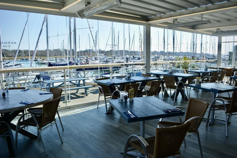 Banana Wharf Hamble's covered terrace on a sunny day, Mermaid Gin branding on the glass sides and boats moored in the marina beyond
